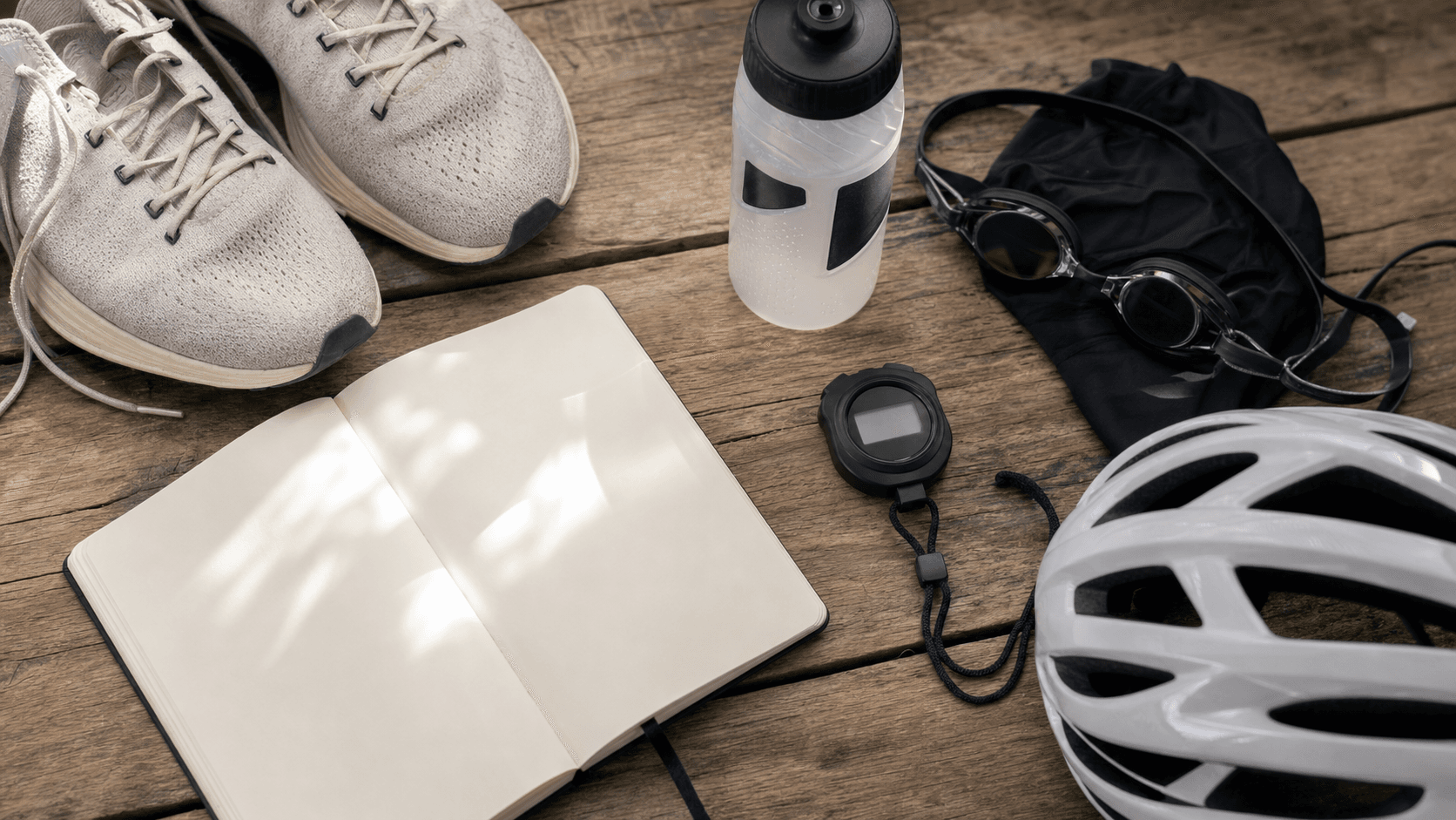 Unbranded triathlon training-planning flat lay with stopwatch, notebook, running shoes and swim goggles